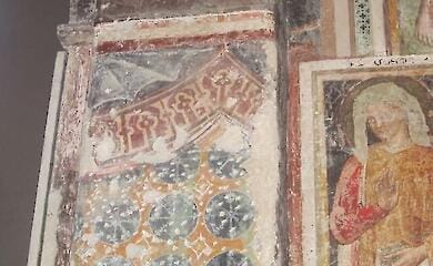 The upper part of a 13th-century fresco showing tent textiles hung on the walls of the apse, with motifs of eight-pointed stars and pseudo-Arabic inscriptions above them. On the right is part of a later fresco added in the fifteenth century.