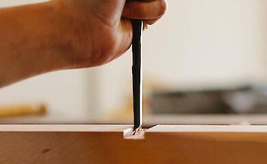 A craftsman’s hand with a chisel working a wooden piece in a workshop.