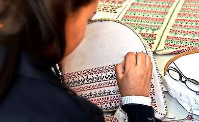 A woman hand-embroiders a red-and-black pattern on fabric stretched over an embroidery hoop.