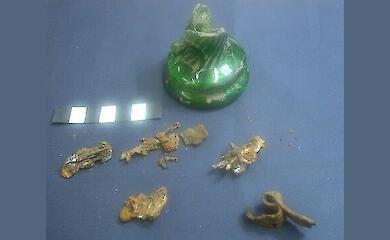 A damaged green glass bottle and rusty metal objects found nearby, on a blue background.