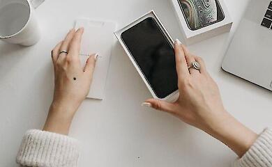 A person places a smartphone into an open cardboard box on a table.