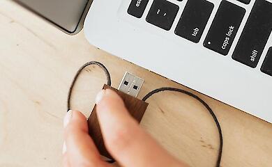 A hand plugging a USB device into the port of an open laptop.