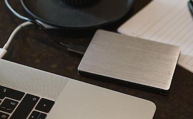 An external drive connected by cable to a laptop on a desk.