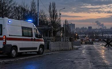 An ambulance stopped at a blocked road with distant smoke in the background