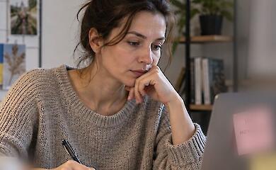 A woman at a desk considers her job search and writes down a plan next to her laptop.