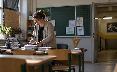 A teacher works with paperwork in a school classroom next to the entrance of a protected shelter
